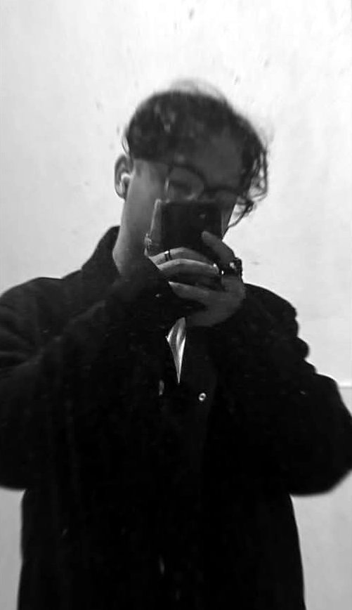 Bibek taking a mirror photo in a black coat, rings and glasses
